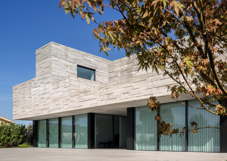 Agrela House, Paredes: board-marked concrete volume cantilevering above floor-to-ceiling glazing, framed by autumn leaves