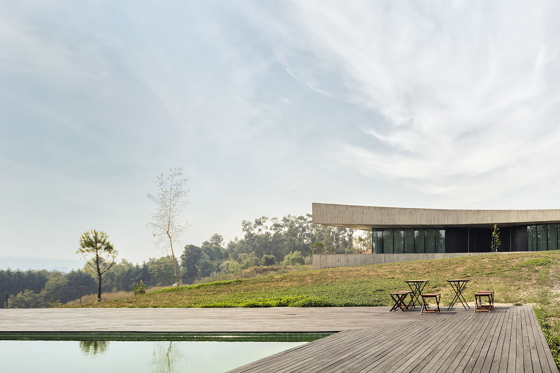 Pool and timber deck with chairs in the foreground, the Cabo de Vila House in Paredes low on the hillside beyond