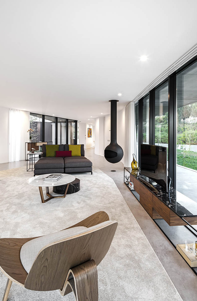 Cabo de Vila House, Paredes: living room with sofa, low furniture and a suspended fireplace beside floor-to-ceiling glazing