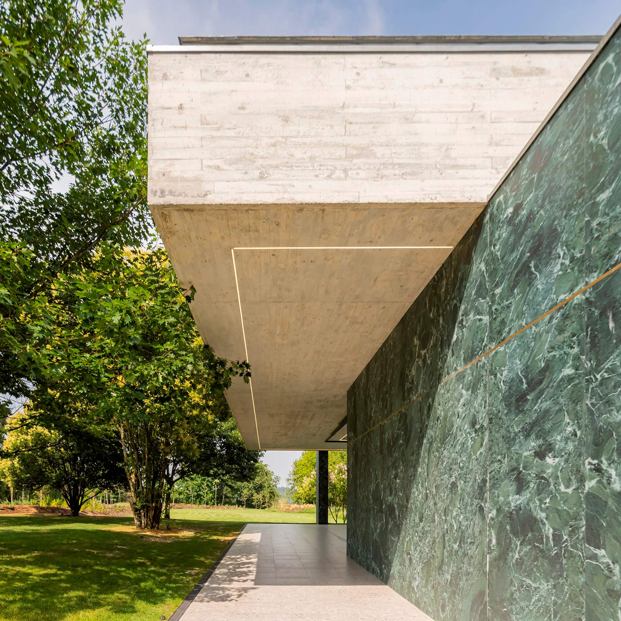 Pavilion in the Garden, Paredes: deep overhang of the concrete roof above a green-veined wall and a path into the garden