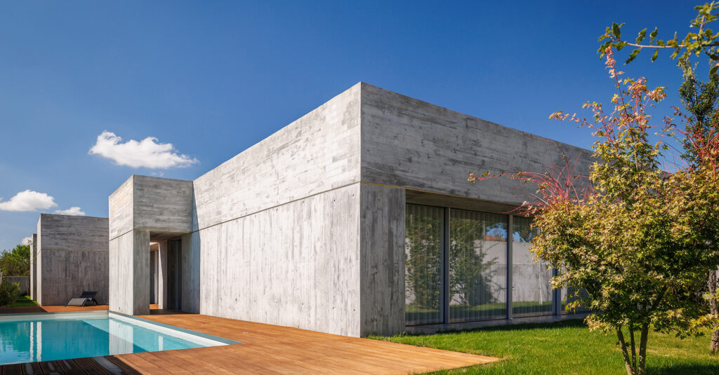 FS House in Paços de Ferreira: board-marked concrete volumes beside the pool, wooden deck and lawn