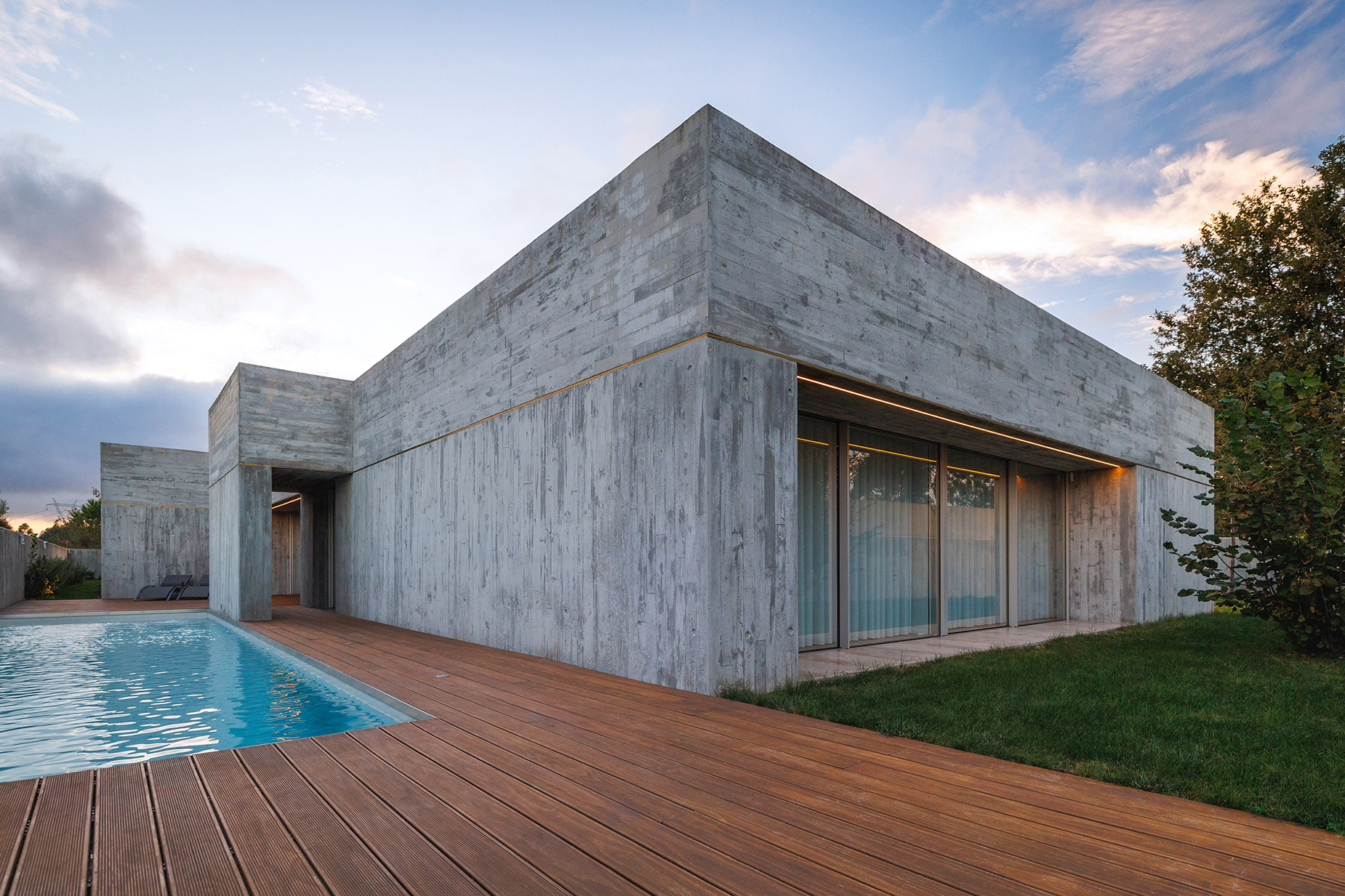 FS House in Paços de Ferreira at sunset, the concrete volume and glazing reflected by the pool and deck