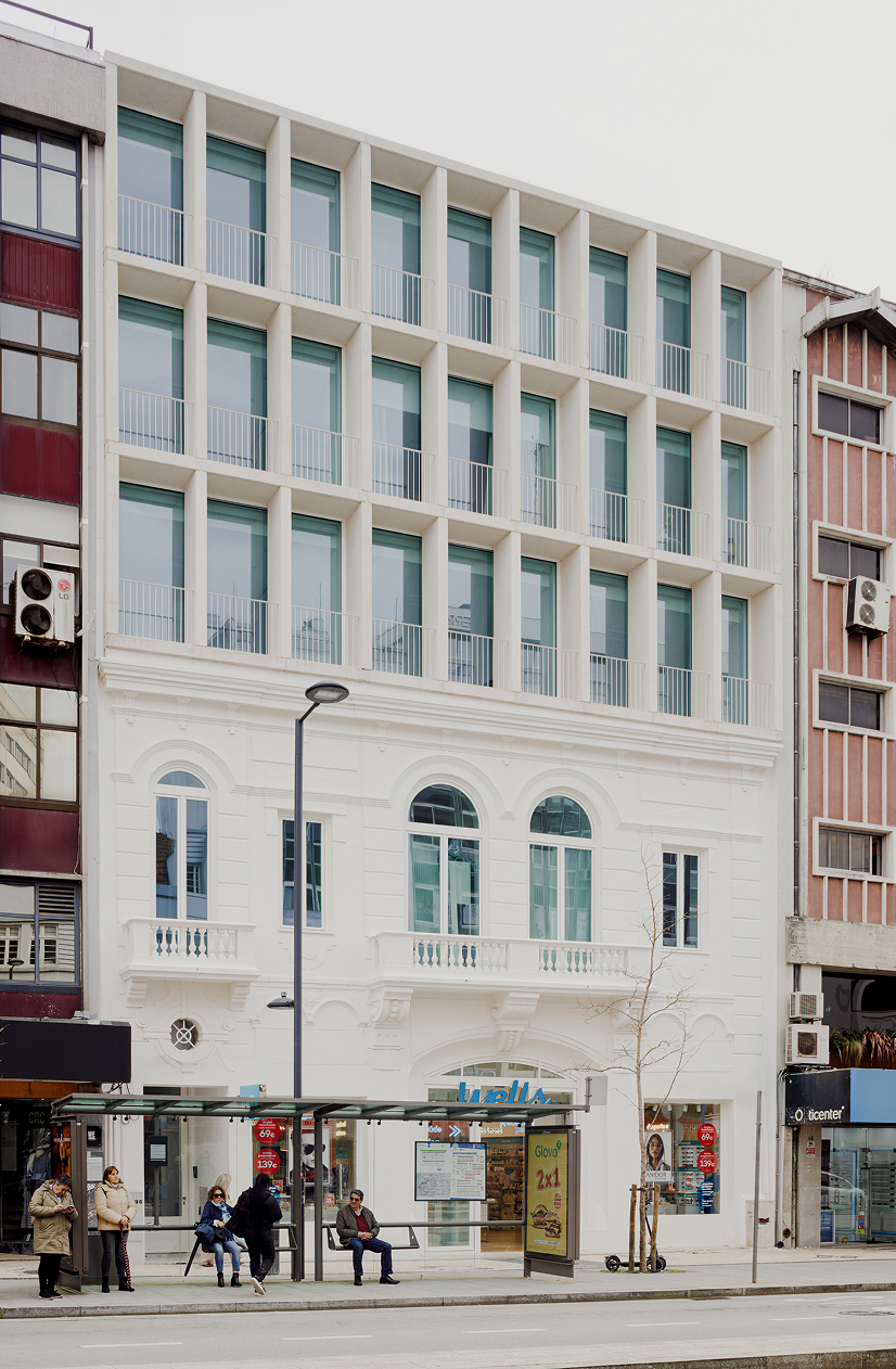 White Aveiro facade with arched ground floor windows and people waiting at the bus stop below