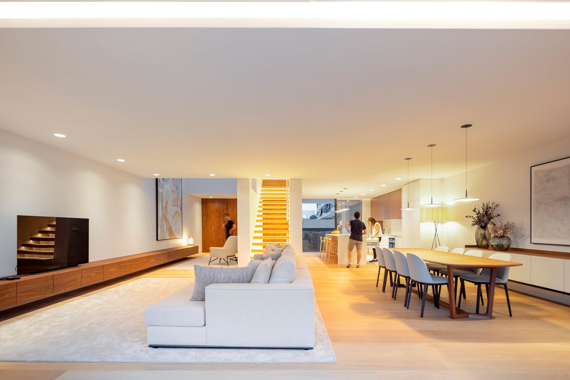 CL2 House, Leça da Palmeira: open-plan ground floor with sofa, dining table and the lit staircase in the background