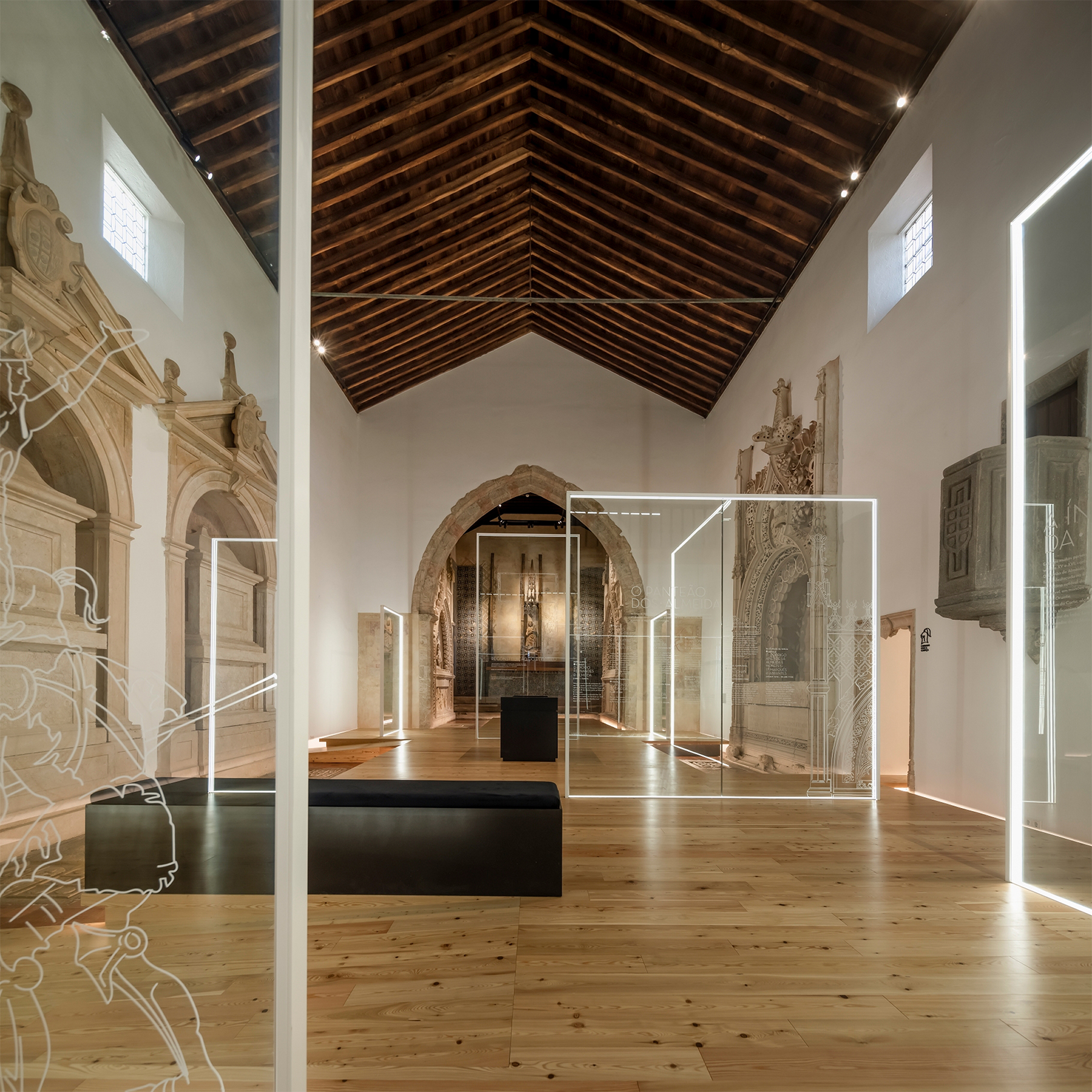 Panteão dos Almeida, Abrantes: black bench between two etched glass panels, with the stone arch and altarpiece beyond