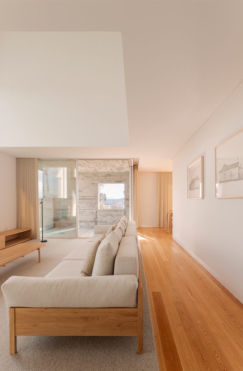 SV House, Sobrado, Valongo: corridor with a sofa and light wood floor leading to a window at the end