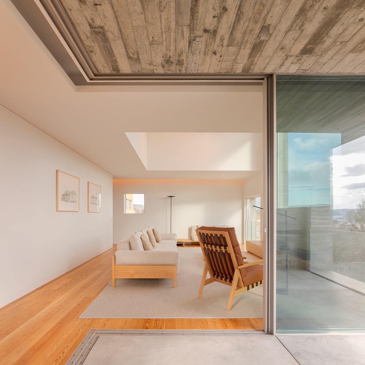 SV House, Sobrado, Valongo: sitting area with a wooden armchair beneath a concrete-framed ceiling opening to the terrace