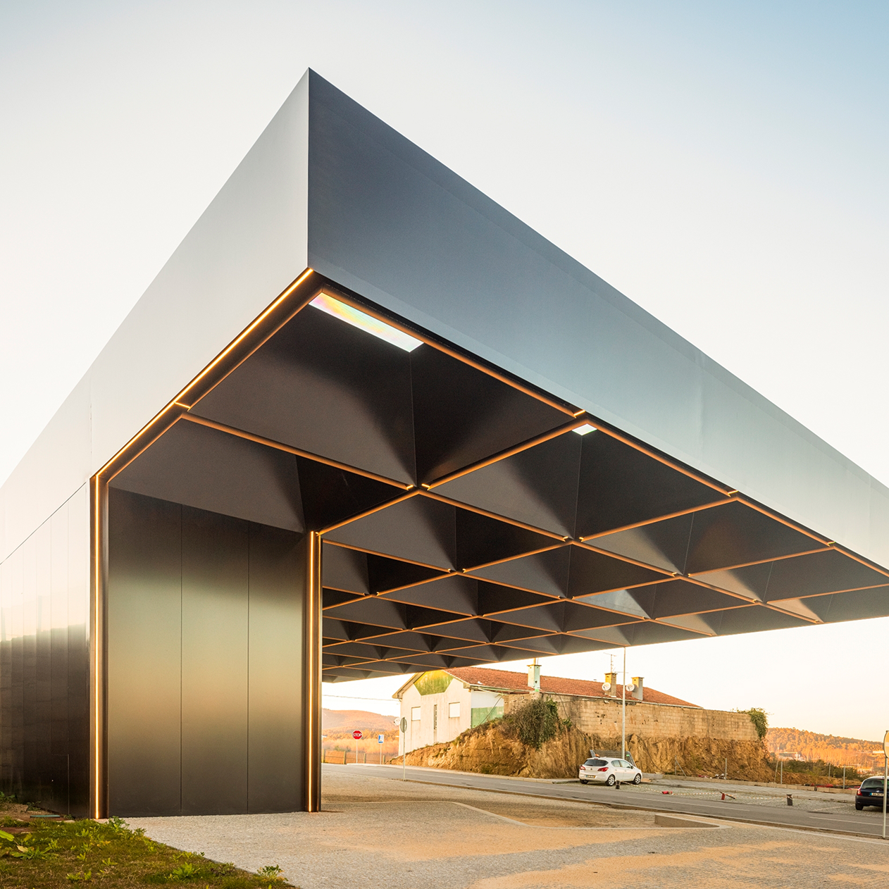 Lousada Intermodal Hub: corner of the roof cantilevering above a dark-clad wall, the coffered soffit lit by afternoon sun