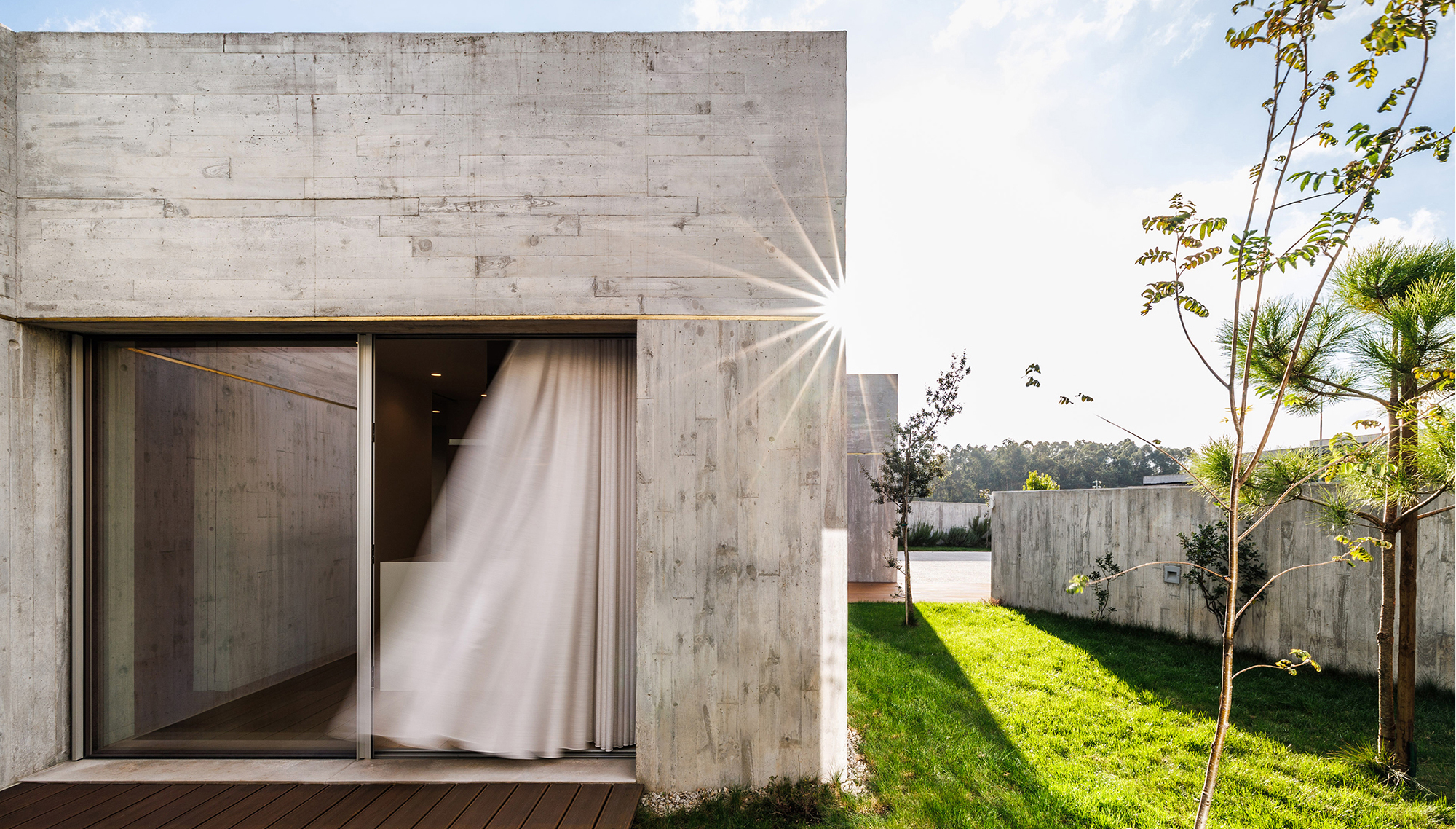 FS House, Paços de Ferreira: glazed corner of the concrete volume with a white curtain caught by the wind