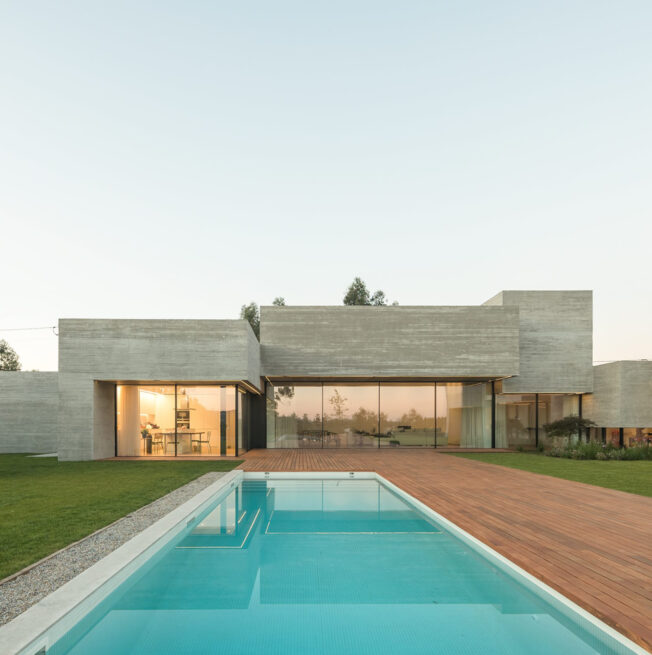 MF House, Paredes: long pool leading to the glazed living room, framed by the board-marked concrete volumes