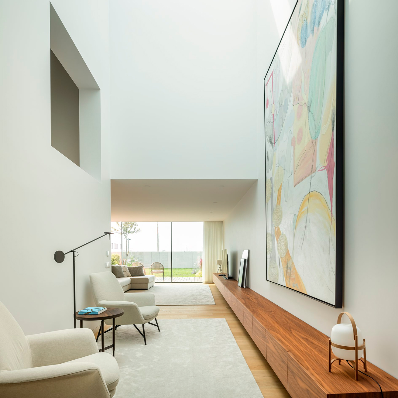 CL2 House, Leça da Palmeira: double-height atrium with armchairs, a large painting and a long low bench, the garden at the end