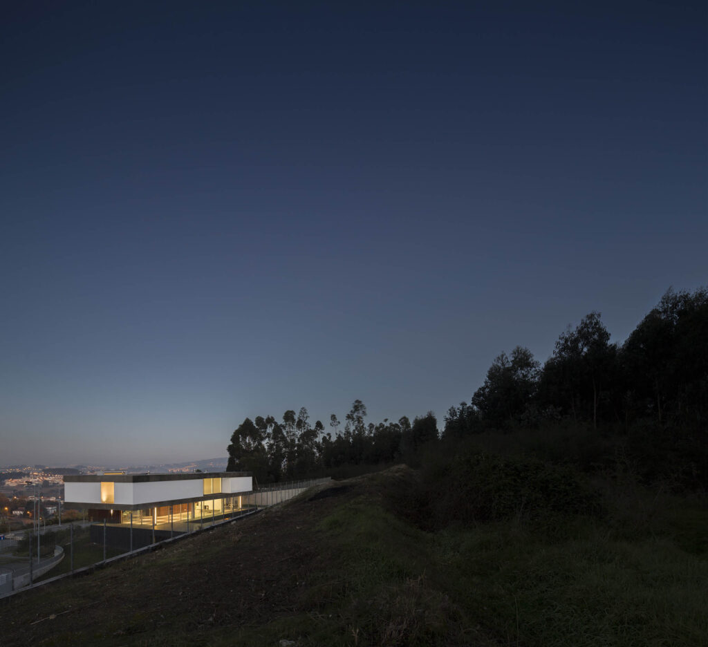 BE House by Spaceworkers at dusk, a low white volume on a hillside