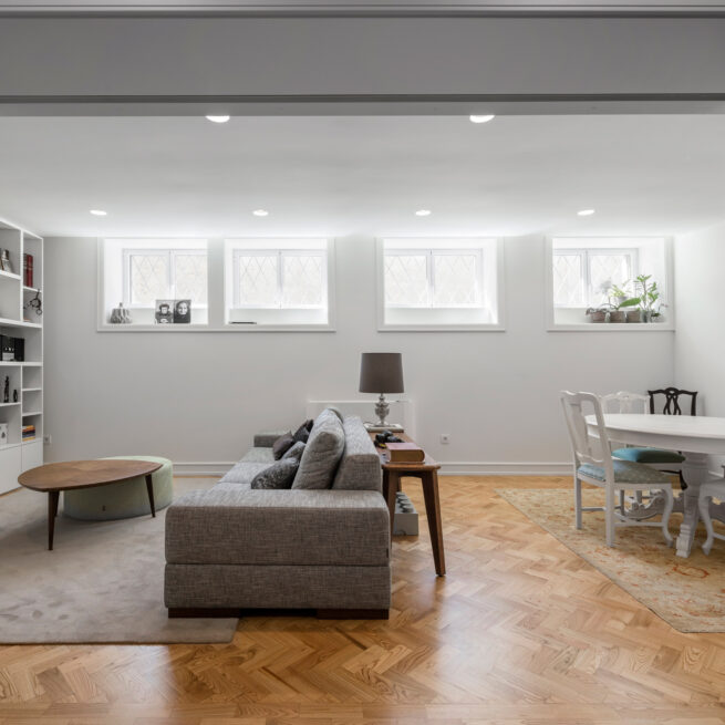 Combatentes House, Porto: lower-floor living room with a grey sofa and a row of high windows