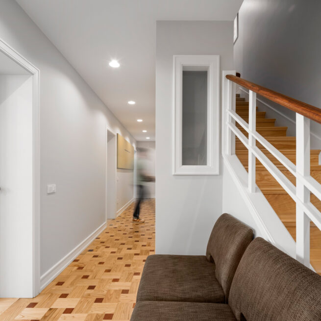 Combatentes House, Porto: upper corridor with a patterned parquet floor beside the staircase and a brown sofa