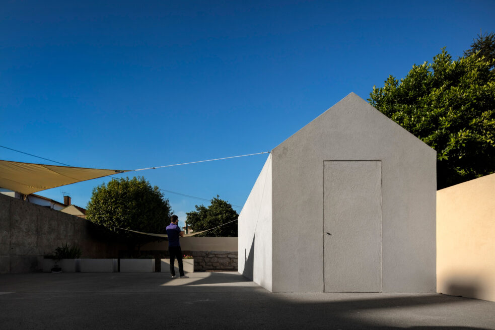 Combatentes House, Porto: grey house-shaped storage annex in the backyard under a blue sky, a figure standing beside it