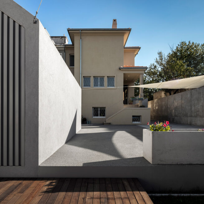 Combatentes House, Porto: backyard seen from the wooden deck, the rear facade beyond a grey wall and a shade sail