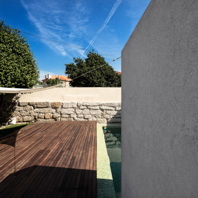 Combatentes House, Porto: wooden deck along the pool beside the grey wall of the annex and an old stone boundary wall