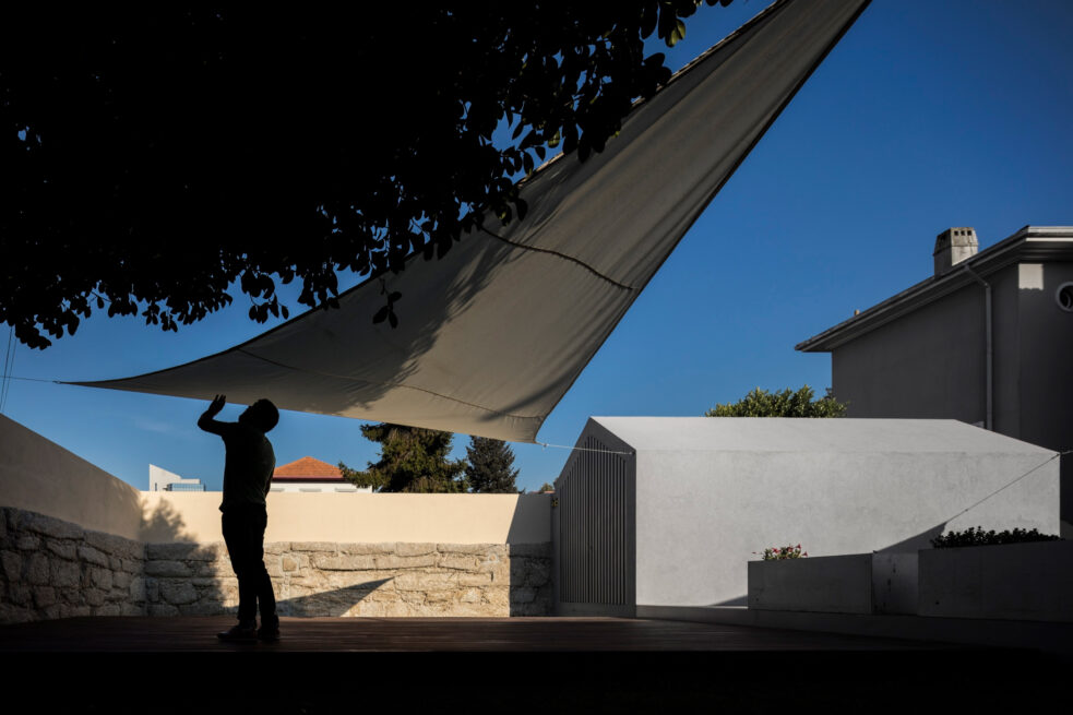 Combatentes House, Porto: silhouette of a person adjusting a shade sail in the backyard, the annex behind